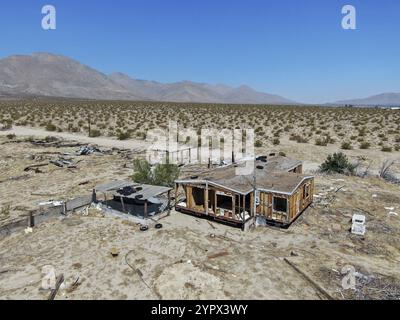 Vista aerea delle case abbandonate e del rimorchio del camper nel mezzo del deserto sotto il cielo blu nel deserto del Mojave in California, vicino a Ridgecrest. Piccolo ro Foto Stock