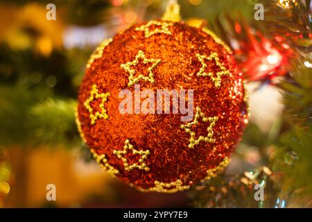 Primo piano di una pallina di Natale rossa decorata con stelle appese su un albero di Natale Foto Stock