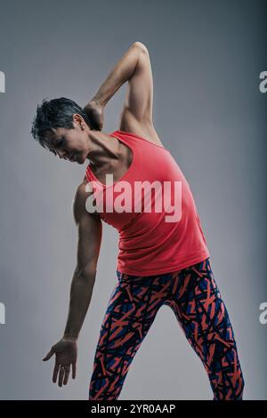 Donna anziana attiva in maglia corallina e leggings si allunga lateralmente, promuovendo flessibilità e benessere Foto Stock