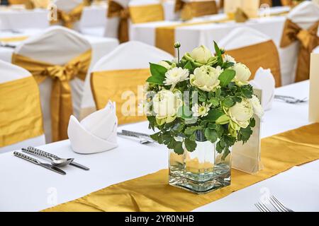 Elegante tavolo per ricevimenti nuziali con centrotavola floreale e decorazioni dorate in una sala banchetti. Foto Stock