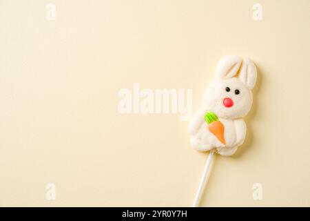 Un grazioso lecca marshmallow a forma di coniglio con una carota arancione, su uno sfondo pastello minimalista Foto Stock