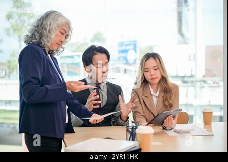 Un gruppo di diversi imprenditori asiatici che lavorano insieme in un ufficio moderno, tutti concentrati sulla discussione, la condivisione di idee e la pianificazione finanziaria Foto Stock
