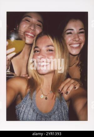 Tre amici sorridenti trascorrono una notte festosa, scattata con un selfie istantaneo con la fotocamera. Foto Stock