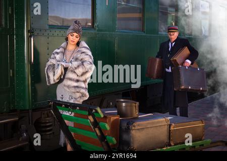 Scena di rievocazione sulla piattaforma vicino a un autentico vagone ferroviario di prima classe 1927 dove una donna di lusso 1920s sta aspettando il suo bagaglio Foto Stock