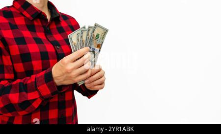banconote da 100 dollari in mano di una persona che indossa una camicia a quadri rossa su sfondo bianco con spazio per le copie. Foto Stock