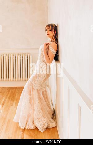Sposa adagiata sul retro contro la parete bianca con un abito da sposa Foto Stock