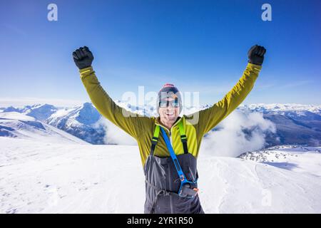 L'uomo solleva le braccia dopo la salita invernale della cima della montagna Foto Stock