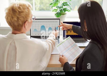 Vista posteriore dei colleghi che utilizzano notebook e grafici in Office Foto Stock