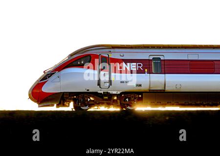 Un treno LNER Azuma (800102), retroilluminato da Un tramonto, mentre viaggia tra le stazioni di Dalmeny e Edinburgh Gateway Scozia Regno Unito Foto Stock