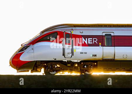 Un treno LNER Azuma (800102), retroilluminato da Un tramonto, mentre viaggia tra le stazioni di Dalmeny e Edinburgh Gateway Scozia Regno Unito Foto Stock