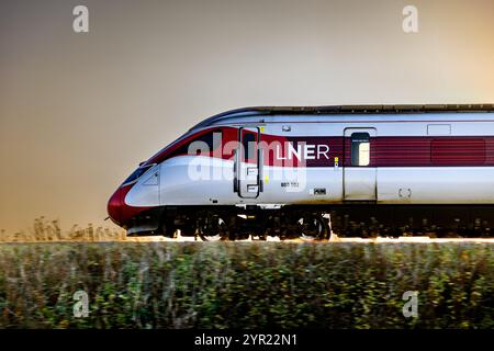 Un treno LNER Azuma (800102), retroilluminato da Un tramonto, mentre viaggia tra le stazioni di Dalmeny e Edinburgh Gateway Scozia Regno Unito Foto Stock