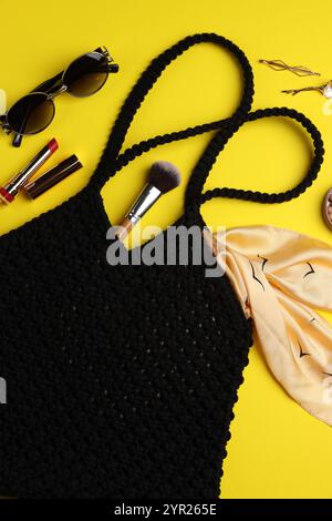 Composizione piatta con sacchetto per la spesa in macrame e prodotti per il trucco su sfondo giallo Foto Stock
