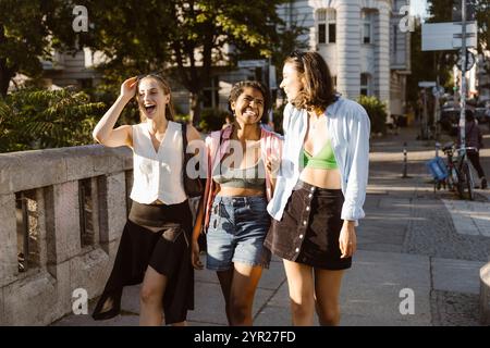 Amiche felici che ridono mentre camminano insieme sul marciapiede Foto Stock