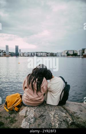 Vista posteriore di un ragazzo adolescente con la testa sulla spalla di un'amica mentre è seduto sulla roccia vicino al mare in città Foto Stock