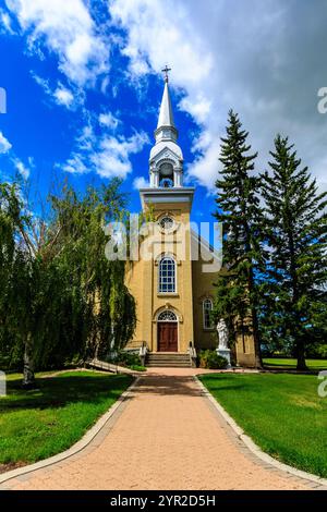 Una grande chiesa con un campanile e una croce in cima. La chiesa è circondata da alberi e ha un passaggio pedonale in mattoni che vi conduce. Il cielo è limpido e blu Foto Stock