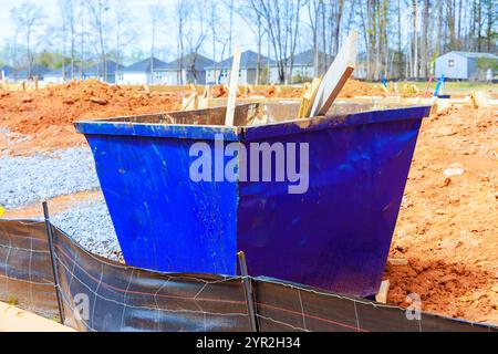 Il dumpster si trova in un cantiere pieno di recinzioni temporanee incorniciate da case lontane durante la costruzione di nuove case Foto Stock