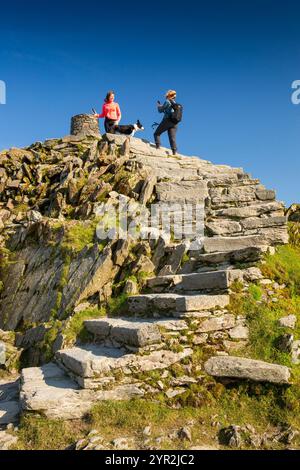 Regno Unito, Galles, Gwynedd, Snowdonia, vetta del Monte Snowdon, camminatori e cane in cairn al trig point Foto Stock