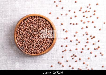 Lenticchie marroni essiccate in una ciotola di legno su tessuto di lino. Lenticchie di montagna non sgusciate con cappotti di semi castani e semi a forma di lente rosso-arancio. Foto Stock