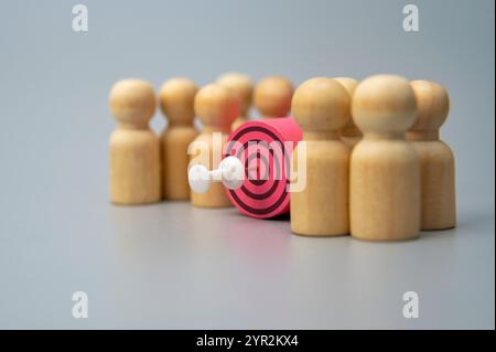 Un bersaglio con un dardo al centro circondato da figure di legno. Concetto del cliente target. Foto Stock