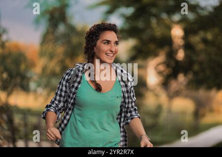 Giovane donna che fa un'escursione felice in un parco lussureggiante, circondato dal verde e dalla luce del sole che filtra tra tra gli alberi, catturando l'essenza di un sano e attivo Foto Stock