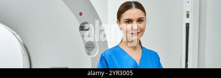 Attraente medico femminile in scrub blu si trova con sicurezza vicino alla macchina per la risonanza magnetica in ospedale. Foto Stock