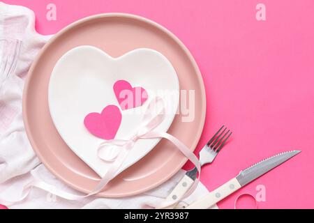 Tavolo per San Valentino con tovagliolo, nastro e cuori di carta su sfondo rosa Foto Stock