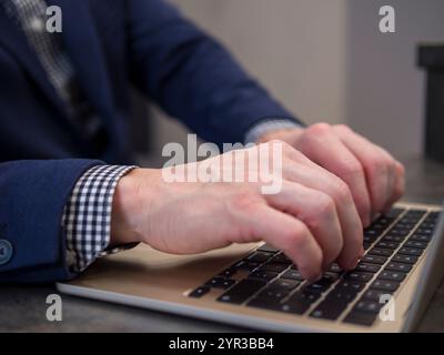Uomo d'affari che scrive sulla tastiera del notebook in ufficio, sottolineando la produttività e la tecnologia sul posto di lavoro Foto Stock
