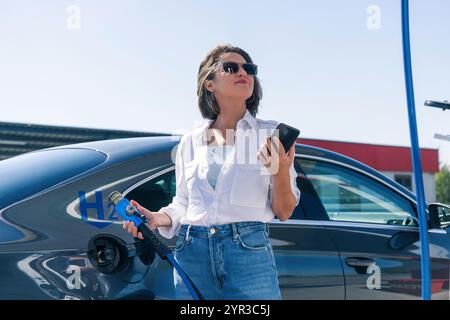 Donna tiene un ugello di alimentazione dell'idrogeno su una stazione di rifornimento dell'idrogeno. Rifornimento di carburante per auto con idrogeno. Foto Stock