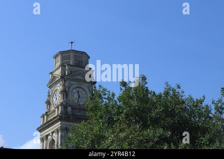 Portsmouth, Hampshire, Inghilterra. 26 agosto 2024. La torre dell'orologio di Portsmouth Guildhall si affacciava da una finestra del treno con cielo blu e cime frondose di alberi. Foto Stock
