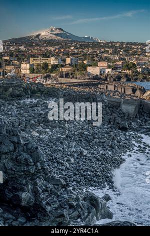 Sopra l'Etna, visto da Ognina, storico porto di pescatori di Catania; in primo piano, le rocce laviche prodotte dal vulcano. Sicilia, Italia. Foto Stock