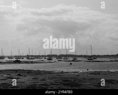 Emsworth, Hampshire, Inghilterra. 26 agosto 2024. Vista in scala di grigi dalla spiaggia delle navi a vela nel porto. Foto Stock