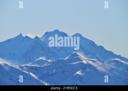 Cime innevate retroilluminate da neve volante, su un cielo azzurro limpido in un paesaggio ventoso, Leukerbad, Leuk, Vallese, Svizzera, Europa Foto Stock