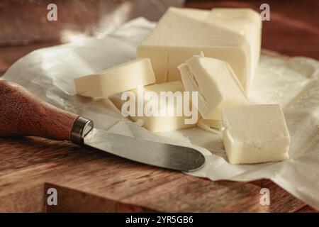 Bricchette di burro, carta da imballaggio, tagliere di legno e coltello da burro, colazione, stile rustico, niente persone Foto Stock