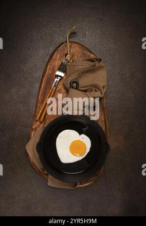 Uova fritte in una padella di ghisa, colazione, uova fritte a forma di cuore, vista dall'alto, niente persone, fatto in casa Foto Stock