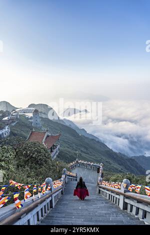 Una donna con una gonna rossa su una scalinata ripida sulla cima del Fansipan, la montagna più alta del Vietnam Foto Stock