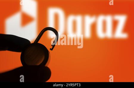 Una mano regge un lucchetto sbloccato davanti al logo Daraz. Foto Stock