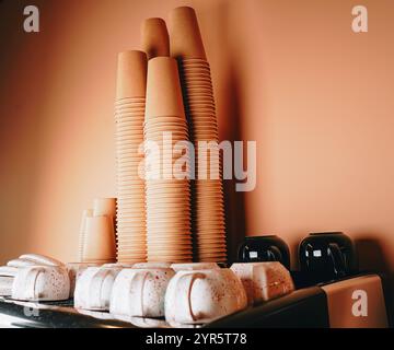 Un gruppo di tazze di carta si siede sulla macchina del caffè e le loro stampe vivaci aggiungono un tocco di colore all'elegante e moderno allestimento del caffè. Foto Stock