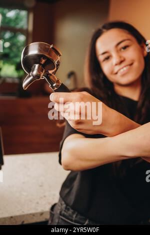 Sorridendo calorosamente, il barista tiene in mano il titolare, creando un cappuccino perfetto per il cliente in attesa. Foto Stock