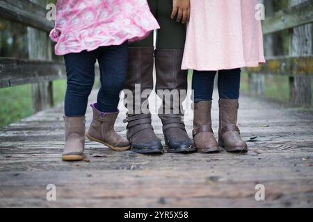Primo piano di genitori e bambini che indossano gli stivali sul ponte di legno Foto Stock