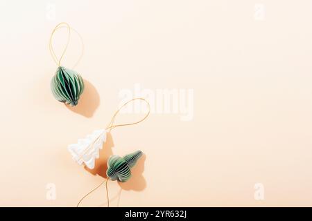 Tre decorazioni natalizie di carta verde e bianca con corde dorate su sfondo beige, vista dall'alto. Copia spazio. Foto Stock