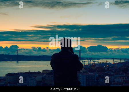 Silhouette del fotografo che scatta foto del bellissimo tramonto su lisbona, portogallo, con l'iconico ponte 25 de abril e il paesaggio urbano Foto Stock