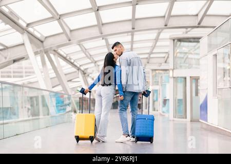 Giovani coppie che condividono un bacio all'aeroporto prima della loro avventura di vacanza Foto Stock