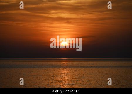 Tramonto mozzafiato sulle calme acque dell'oceano con il vibrante cielo arancione Foto Stock