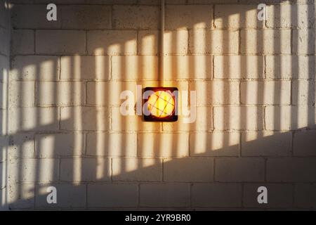 Una lampada da parete gialla su una parete in mattoni con un'ombra a motivi geometrici Foto Stock