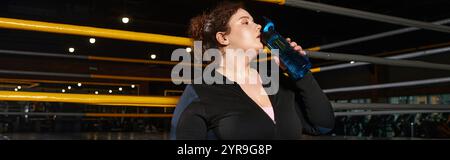 Una donna dedicata fa una pausa per idratarsi mentre è impegnata in una vigorosa routine di allenamento in palestra. Foto Stock