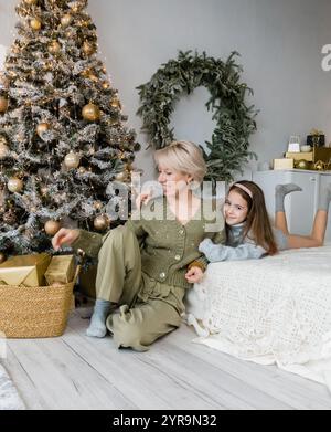 Una madre e una figlia condividono un momento tenero vicino a un albero di Natale splendidamente decorato. Avvolti in comodi maglioni, emanano calore e allegria durante le vacanze Foto Stock