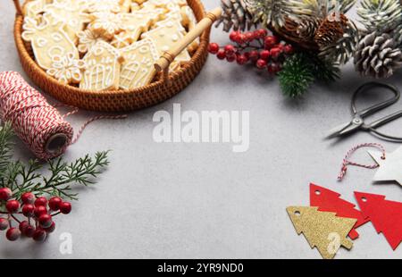 Composizione natalizia con biscotti al pan di zenzero, coni di pino, ornamenti e forniture artigianali su sfondo grigio, che evocano una vacanza calda e festosa Foto Stock