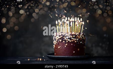 Torta al cioccolato decorata con molte candele d'oro per il compleanno e scintillanti Foto Stock