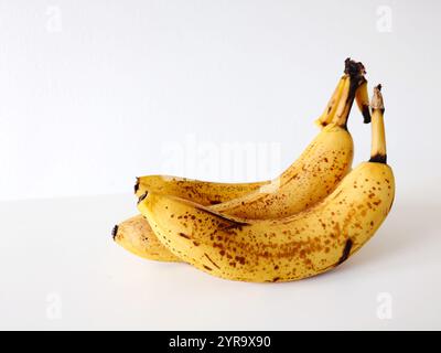 Banane crude macchiate e macchiate con punti neri e macchie. Primo piano, grandangolo, isolato sul bianco, nessuna gente. Foto Stock