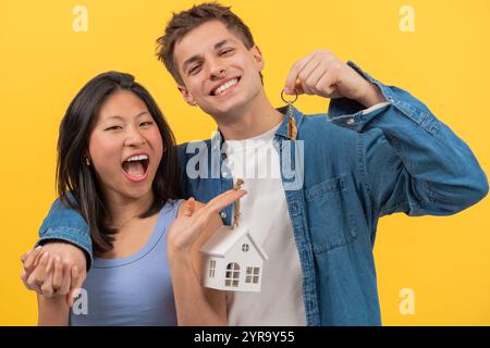 Coppia felice che tiene in mano le chiavi di casa e una piccola casa modello, per celebrare la nuova casa Foto Stock